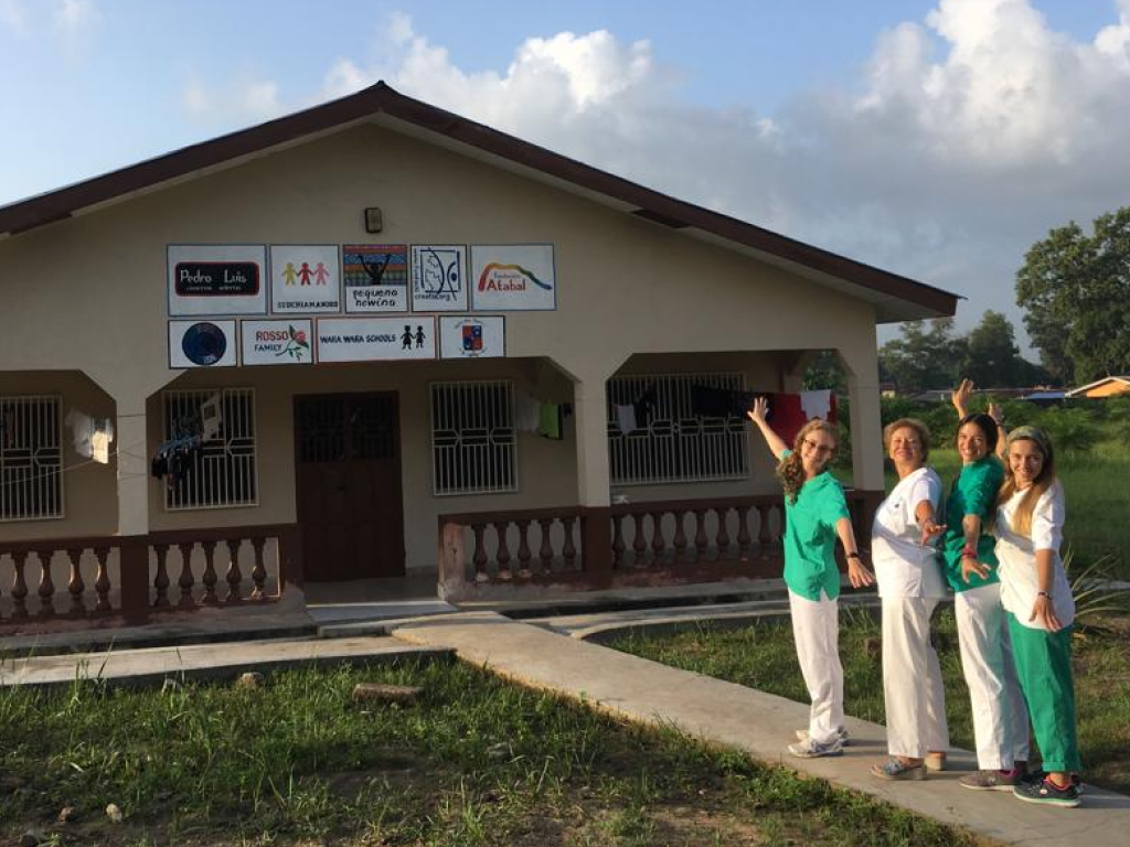4 voluntarias vestidas de sanitarias delante de una casa